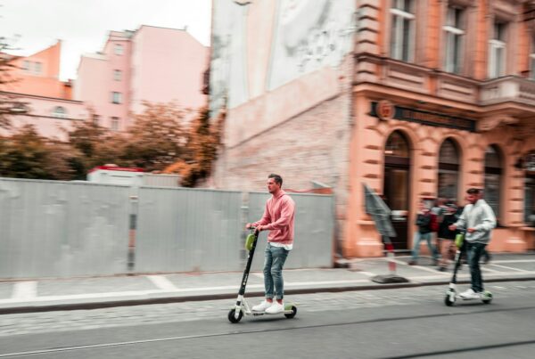 two men riding kick scooters during daytime